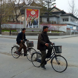 North Koreans cycle past a propaganda poster (Getty)